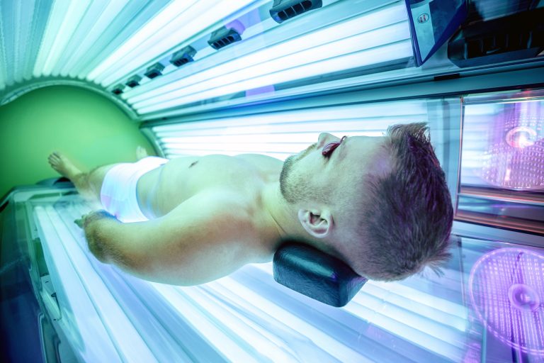 Attractive muscular man in a sunbed with protective uv glasses